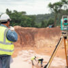 Topógrafo em obra usando equipamento de medição em terreno.