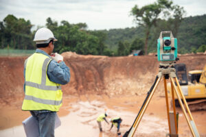 Topógrafo em obra usando equipamento de medição em terreno.