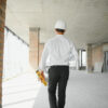 Profissional de engenharia usando capacete de segurança caminha por obra em construção enquanto realiza inspeção do espaço.