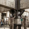 Engenheiros e técnicos executam reforço estrutural em pilar de concreto com perfis metálicos em obra de retrofit.